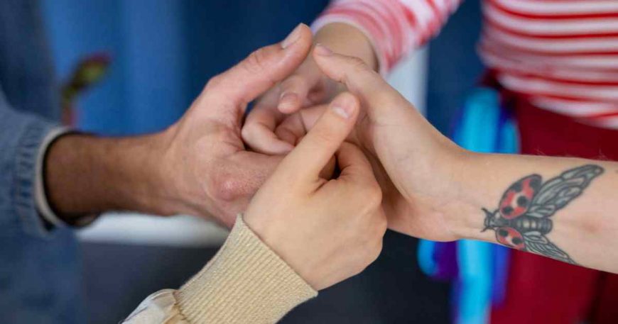 Four people join hands as one, with thumbs up and fingers swirled together.